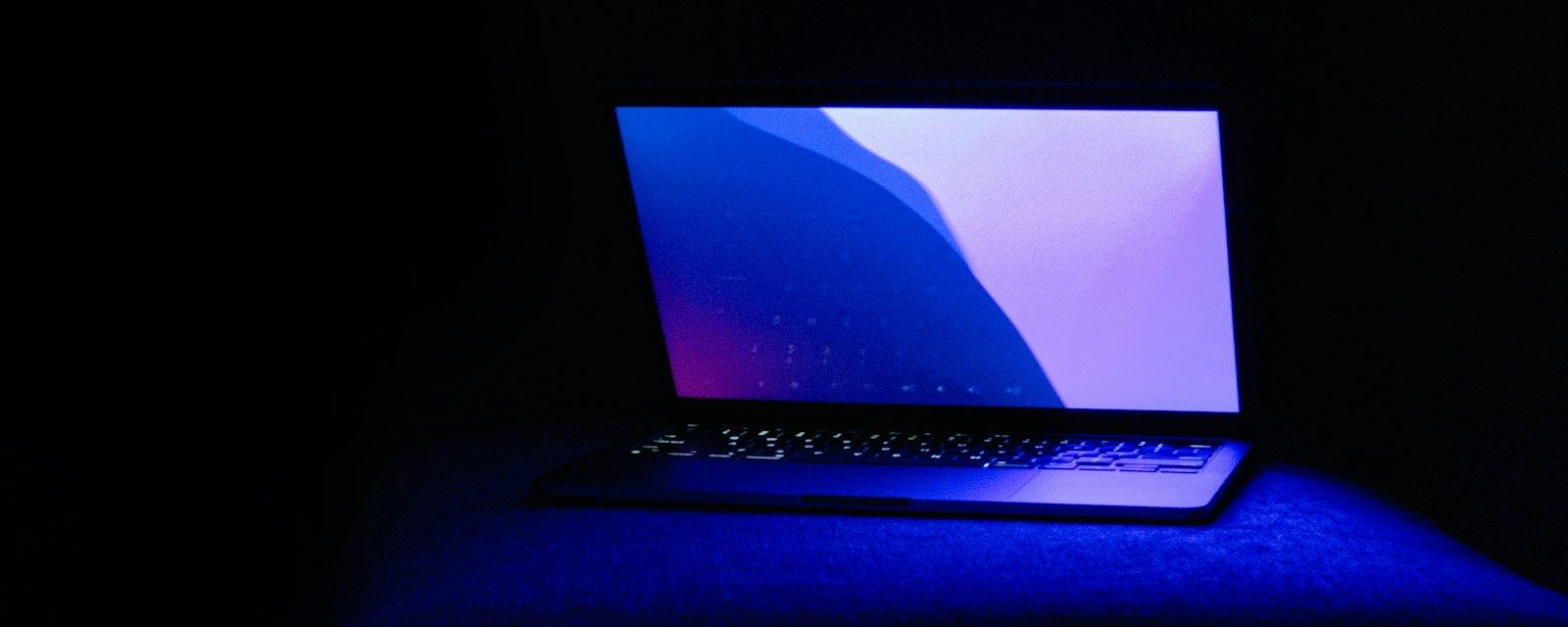 An open laptop glowing blue in a dark room